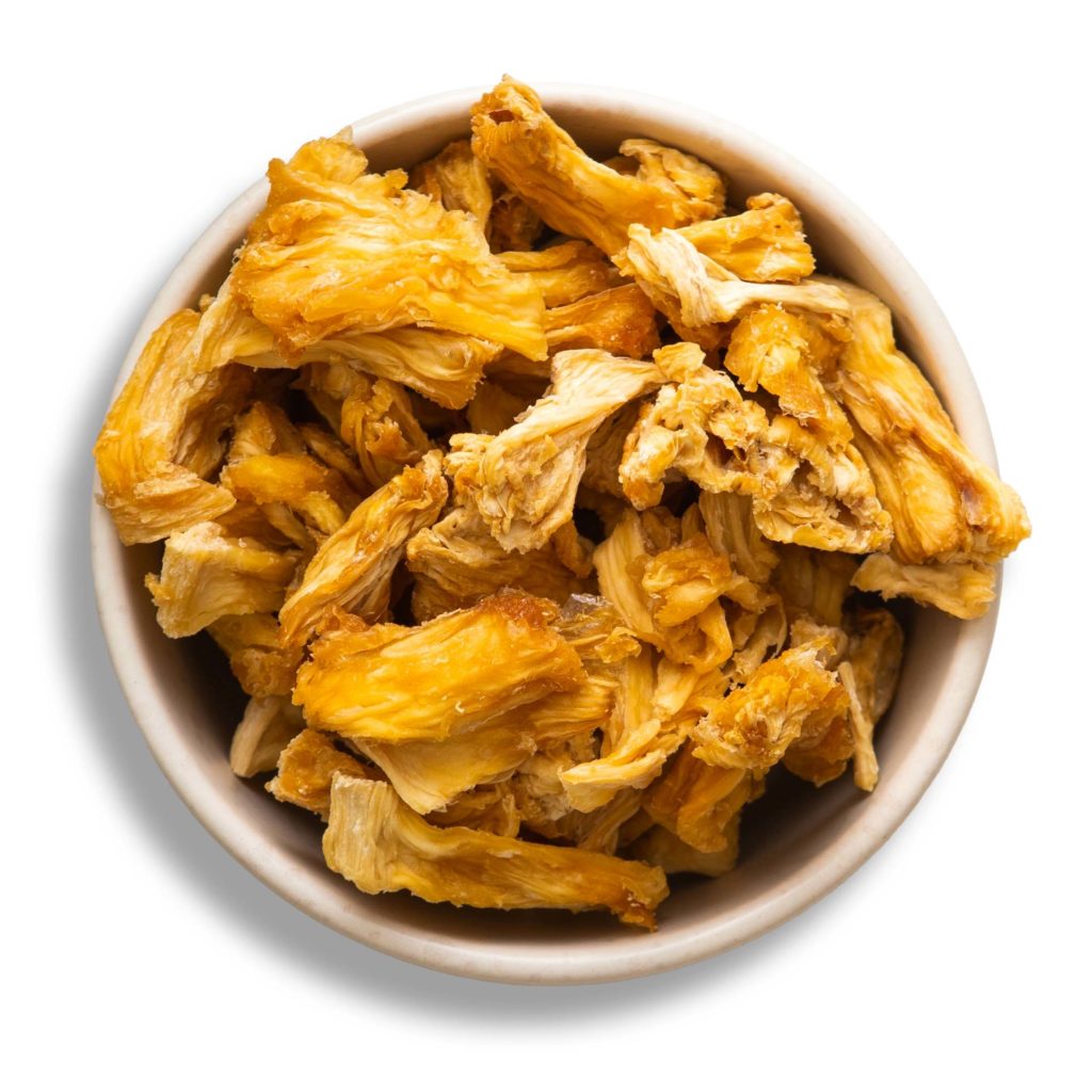 Una ciotola bianca piena di pezzi sminuzzati di ananas disidratato giallo-dorato, apprezzato per le sue proprietà, vista dall'alto.