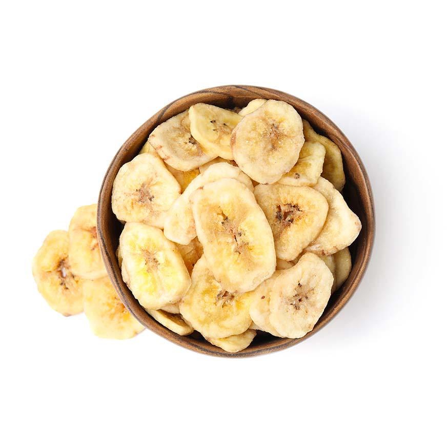 Fette di banana essiccata leggermente dorate e croccanti in una piccola ciotola bianca a forma quadrata.