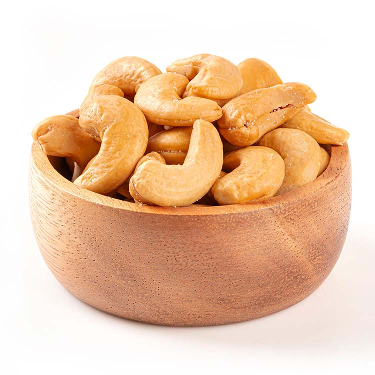 Primo piano di una ciotola di legno naturale ricolma di anacardi dorati e a forma di rene, che risaltano su uno sfondo bianco.