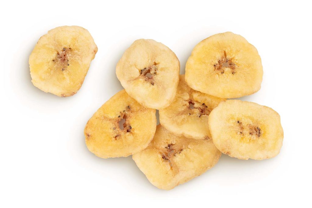 Un mucchio di fette dorate e croccanti di banana essiccata, isolate su sfondo bianco