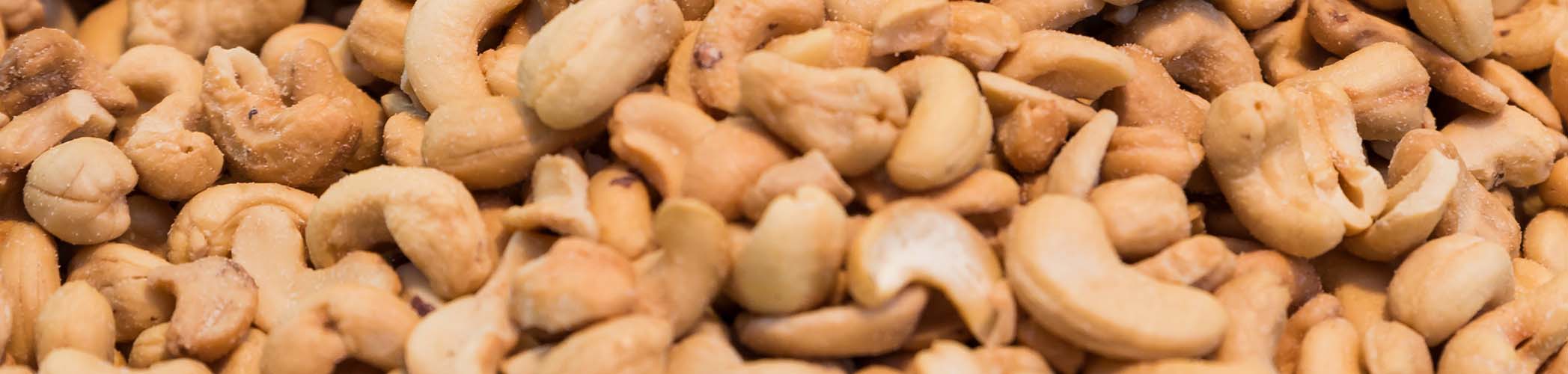 Panoramica ravvicinata e orizzontale di una grande quantità di anacardi tostati, che ne mostra la texture e il colore dorato.