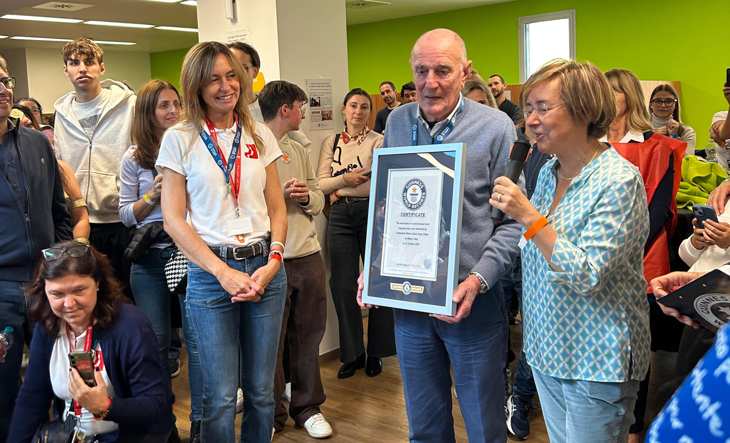Gruppo numeroso di persone, inclusi volontari e famiglie, che partecipano all'evento Guinness World Record 'Batti le mani' per la Fondazione Maria Letizia Verga, con il supporto di Pro. Scena di gioia e solidarietà per la ricerca sulla leucemia infantile.